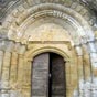 Collgiale de Pimbo:    Le portail sculpt fin XIIe sicle s'ouvre en avance avec un petit toit, sur un puissant mur pignon ajour de deux arcades portant deux cloches, et coiff du chemin de ronde. Une dcoration nave et faussement primitive juxtapose des disques d'allure celtique, des pommes de pins, et des personnages assis et parfois enlacs. 