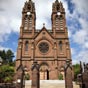 Espalion :  la fin du XIXe sicle, l'glise tant devenue trop petite, un nouvel difice est mis en chantier par le chanoine Brvier. Commence en 1879, la nouvelle glise est consacre le 3 octobre 1880 et reste sous le vocable de St Jean-Baptiste, l'ancienne glise tant dsaffecte. La nouvelle glise paroissiale est une glise  couronnement en grs rouge, dote de 2 tours surmontes des statues de la Vierge et de Saint Joseph de 6 m en bronze. Elle est l'uvre de l'architecte ruthnois Grinda.