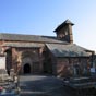L'glise de Perse est difie en grs rose, de style roman trs pur : coeur et absidiole datent du XIme sicle, le reste du XIIme, sauf la chapelle Nord qui est de 1741. Le clocher-mur  quatre arcades se dresse sur l'arc triomphal. Sur le portail nord, parent de celui de Conques : en haut la Pentecte, au dessous Apocalypse et Jugement dernier,  gauche une Adoration des Mages et, peut tre, sur le cordon de l'archivolte, Charles Martel. A l'intrieur sur les chapiteaux : Christ enseignant, combat de chevaliers et de fantassins, oiseaux antithtiques. Une dalle carolingienne a t remploye dans le transept. Chevet appuy sur huit contreforts et orn d'arcatures en plein cintre.
